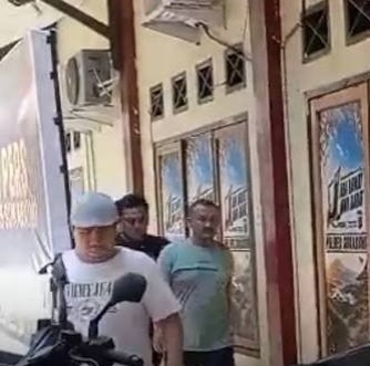 Petugas Unit PPA Satreskrim Polres Sukabumi mengawal seorang pria berkaus hijau sage masuk ke dalam gedung pemeriksaan.